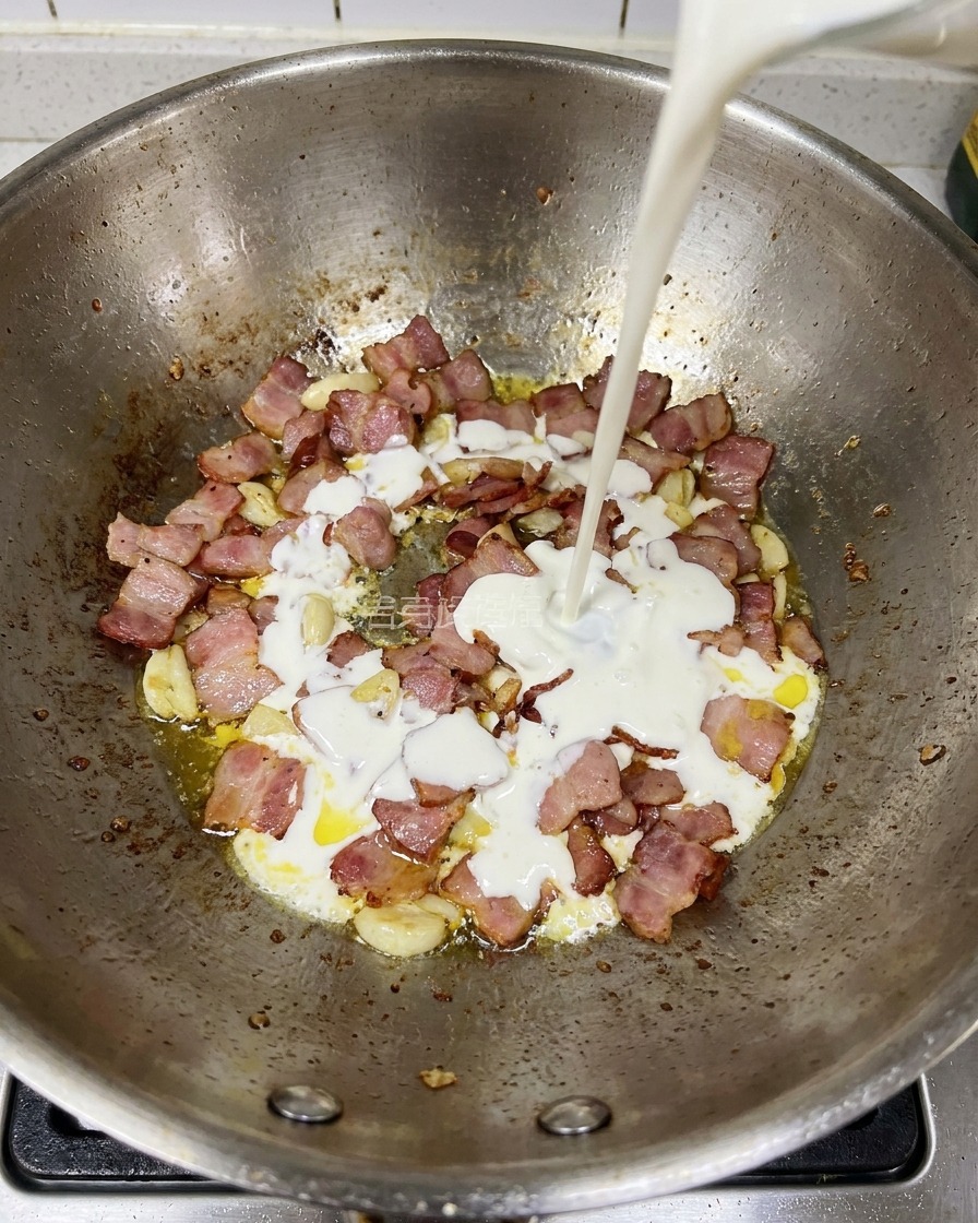 Schlagsahne wird in die Pfanne mit den gebratenen Speck- und Knoblauchstücken gegossen.