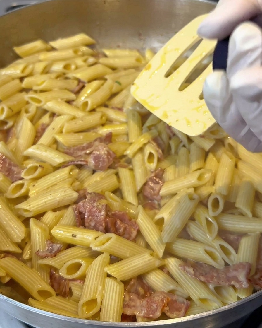 Zitronensalz wird über die cremige Penne-Pasta gemahlen, während sie umgerührt wird.