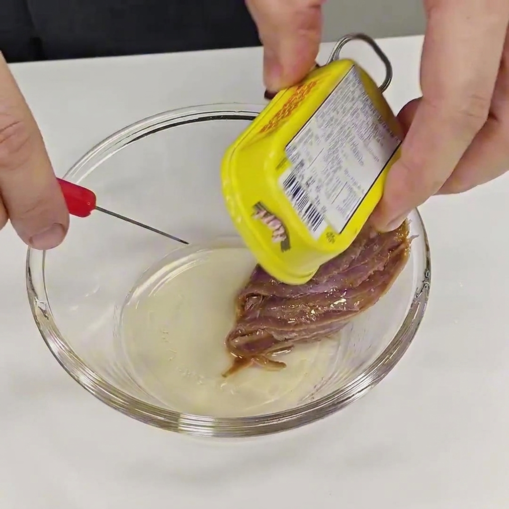 Hände, die ein Sardellenfilet vorsichtig aus einer Dose in eine kleine Glasschale legen.