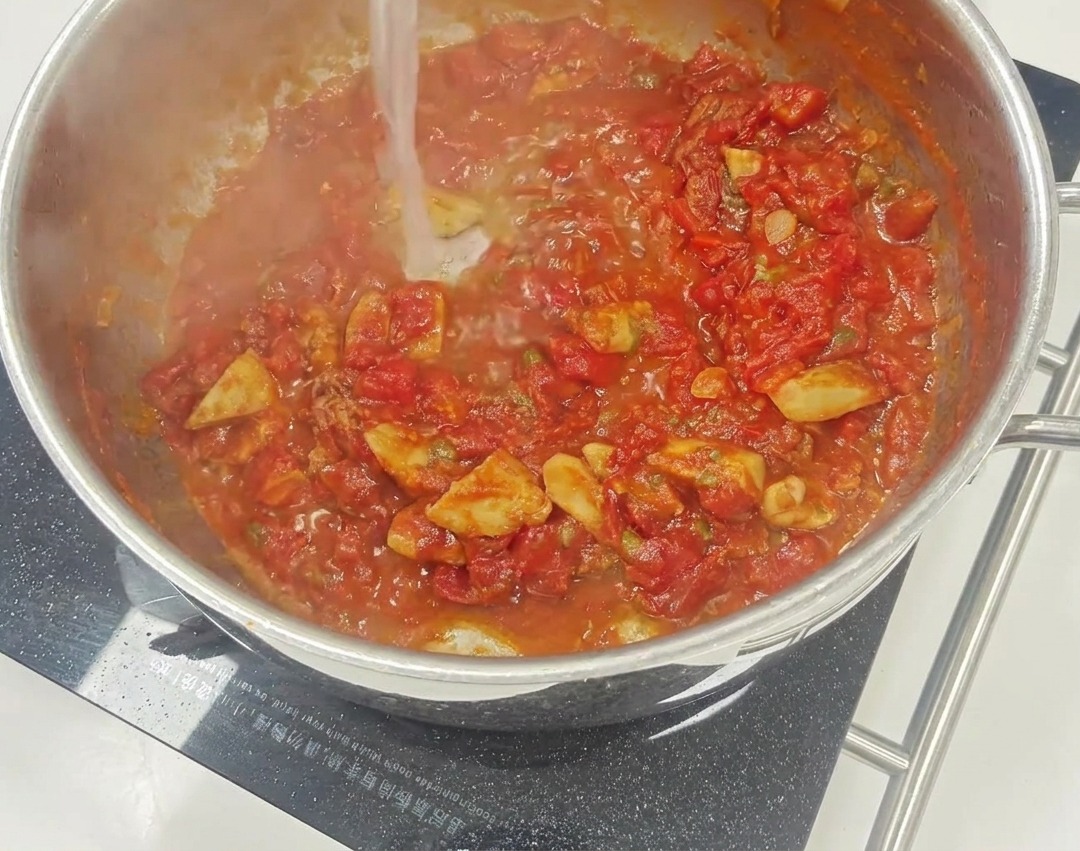 Eine leuchtend rote Tomatensauce, die in einer Pfanne köchelt, mit sichtbaren Stücken von getrockneten Tomaten und Kapern.