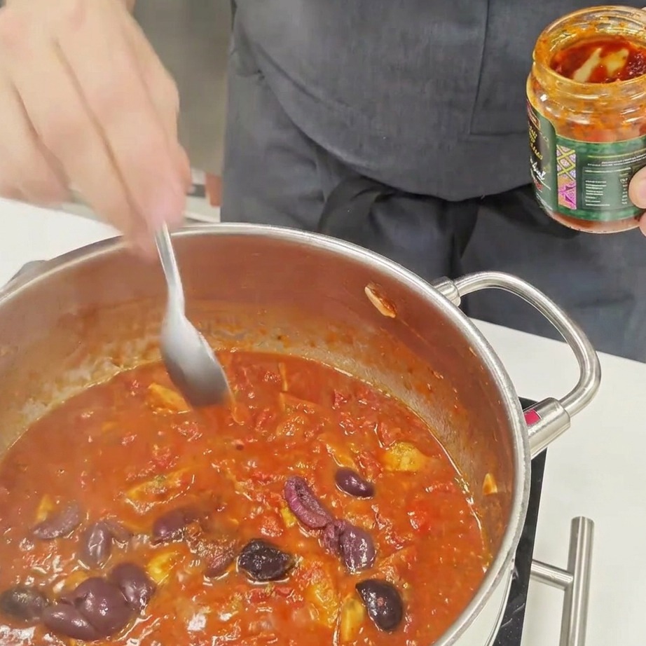 Ein Löffel Chilisauce, der in eine köchelnde Tomatensauce gerührt wird.