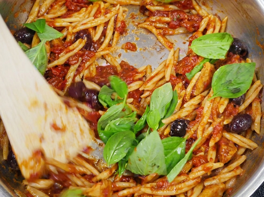 Fertige Trofie-Pasta, vermengt mit Puttanesca-Sauce und garniert mit frischen grünen Basilikumblättern.