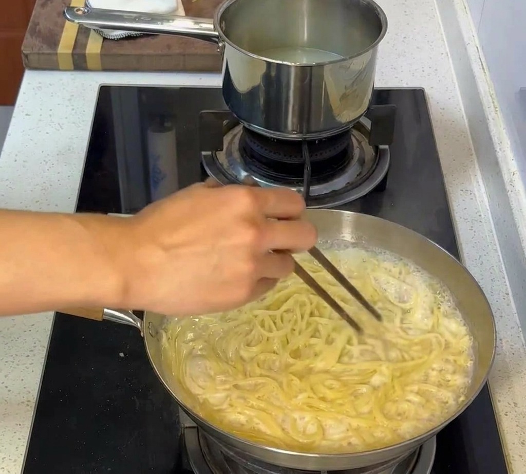 Pasta wird mit Essstäbchen in einer cremigen Sauce geschwenkt, sodass jede Nudel gut bedeckt ist.