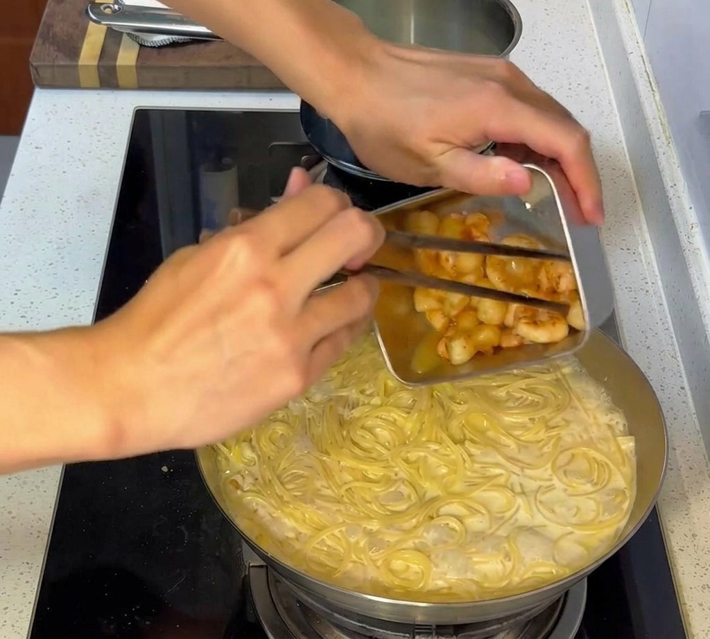 Angebratene Meeresfrüchte werden in die Pfanne mit der vermengten cremigen Pasta gegeben.