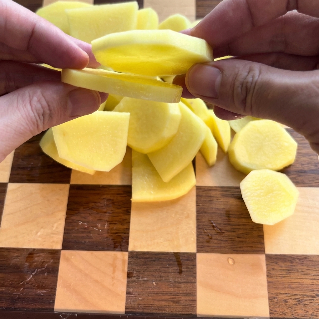Geschälte Kartoffeln werden sorgfältig in Scheiben auf einem Holzbrett geschnitten.