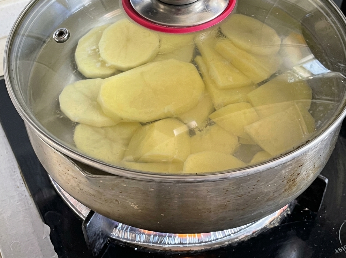 Kartoffelscheiben köcheln in einem Topf mit Wasser auf dem Herd.