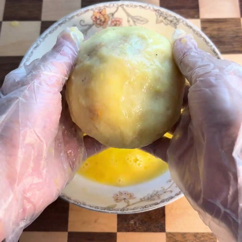 Der Kartoffelkloß wird in einer Schüssel mit verquirltem Ei gewendet.