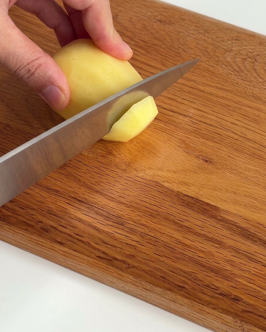 Dünn geschnittene rohe Kartoffelscheiben, ordentlich auf einem Holzbrett arrangiert.
