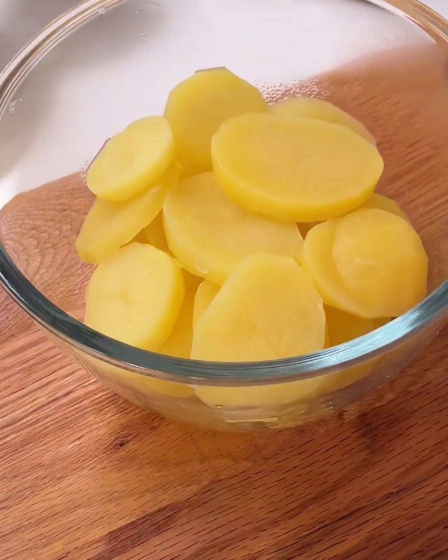 Gedämpfte Kartoffelscheiben in einer Schüssel mit schwarzem Pfeffer und weißer Stärke bestreut.