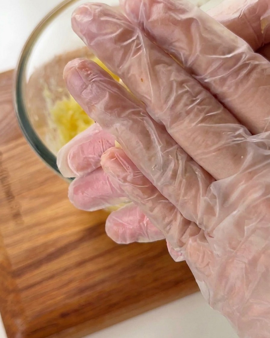 Hände mit Handschuhen formen Kartoffelmasse zu einer kleinen schalenartigen Törtchenform.