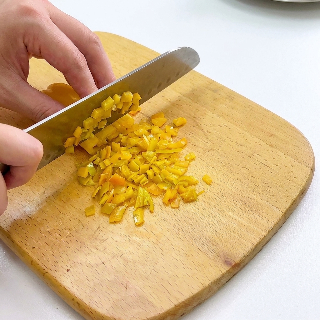 Paprika und Zwiebeln werden fein gewürfelt auf einem Holzschneidebrett.