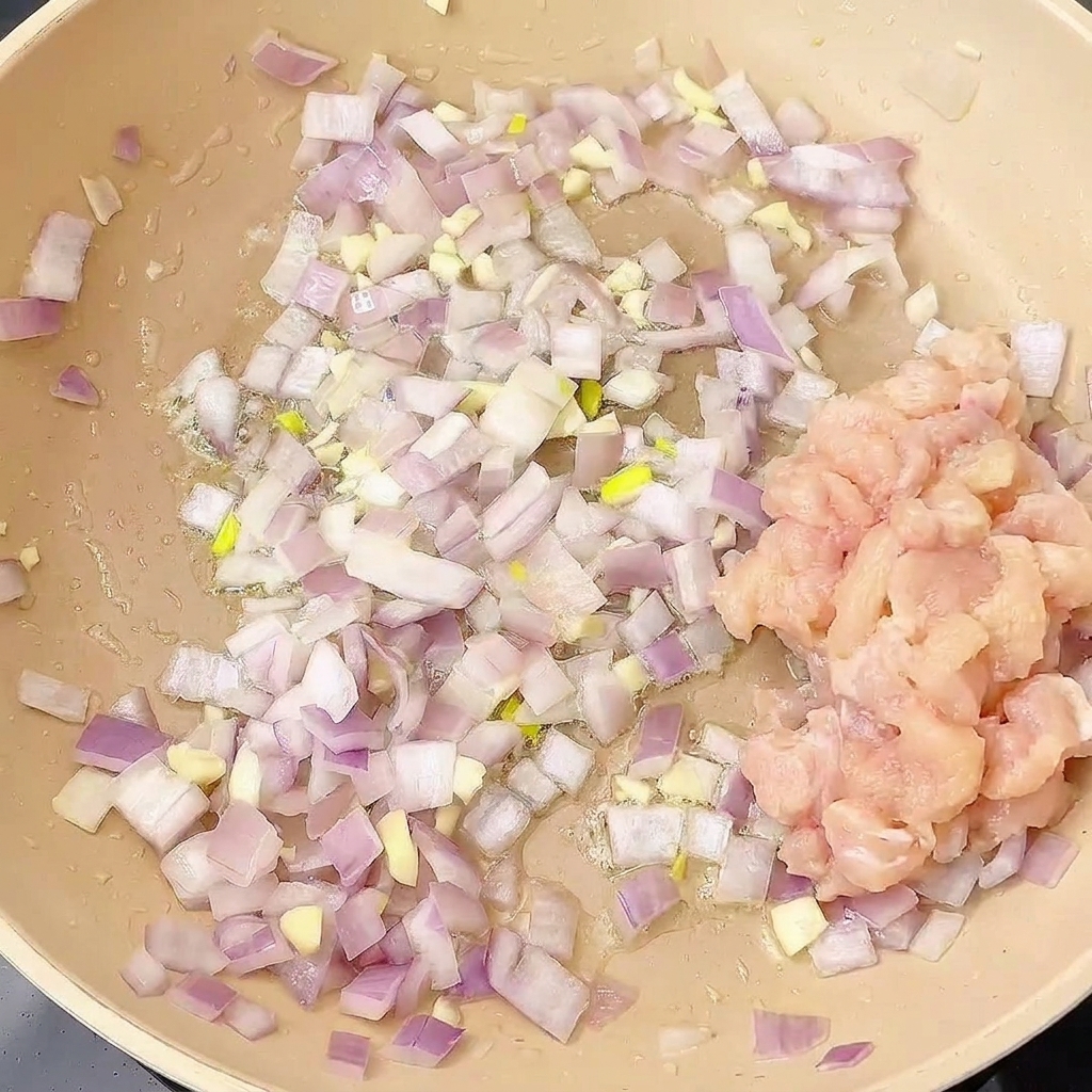 Gewürfeltes Hähnchen wird in die Pfanne zu den gebratenen Zwiebeln und Knoblauch gegeben.
