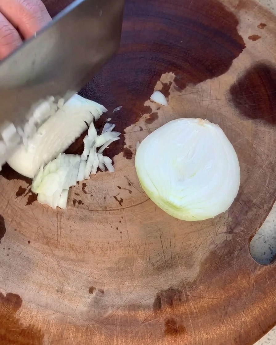 Eine gelbe Zwiebel wird auf einem rustikalen Holzbrett in kleine, gleichmäßige Stücke geschnitten.
