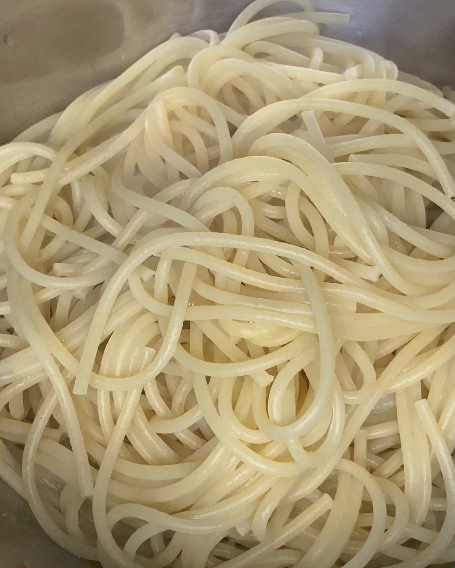 Gekochte Spaghetti werden in einer Edelstahlschüssel mit einem Schuss Olivenöl vermengt.