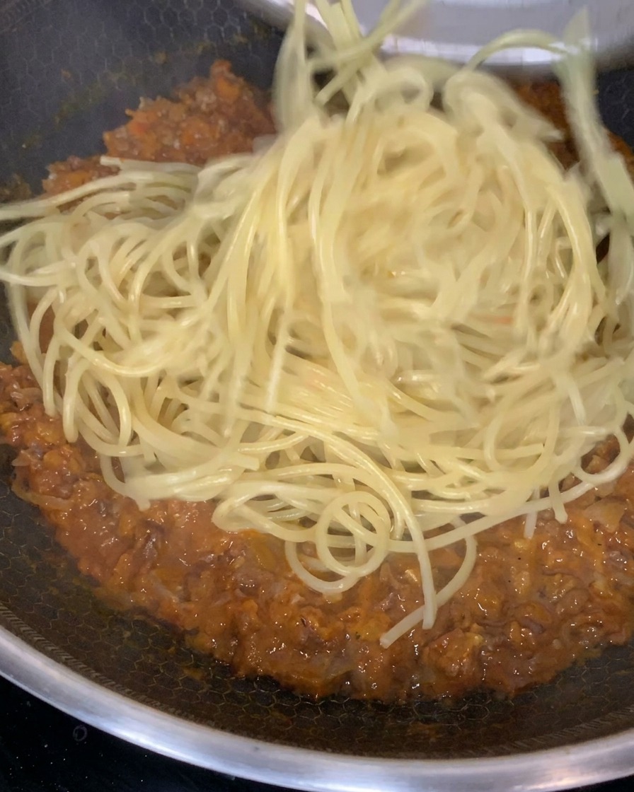 Gekochte Pasta wird in einer großen Pfanne unter die dickflüssige Fleischsauce gehoben.