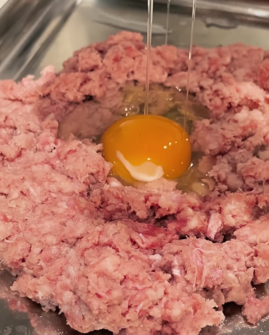 Ein rohes Ei wird über einer Schüssel mit Rinderhackfleisch aufgeschlagen.