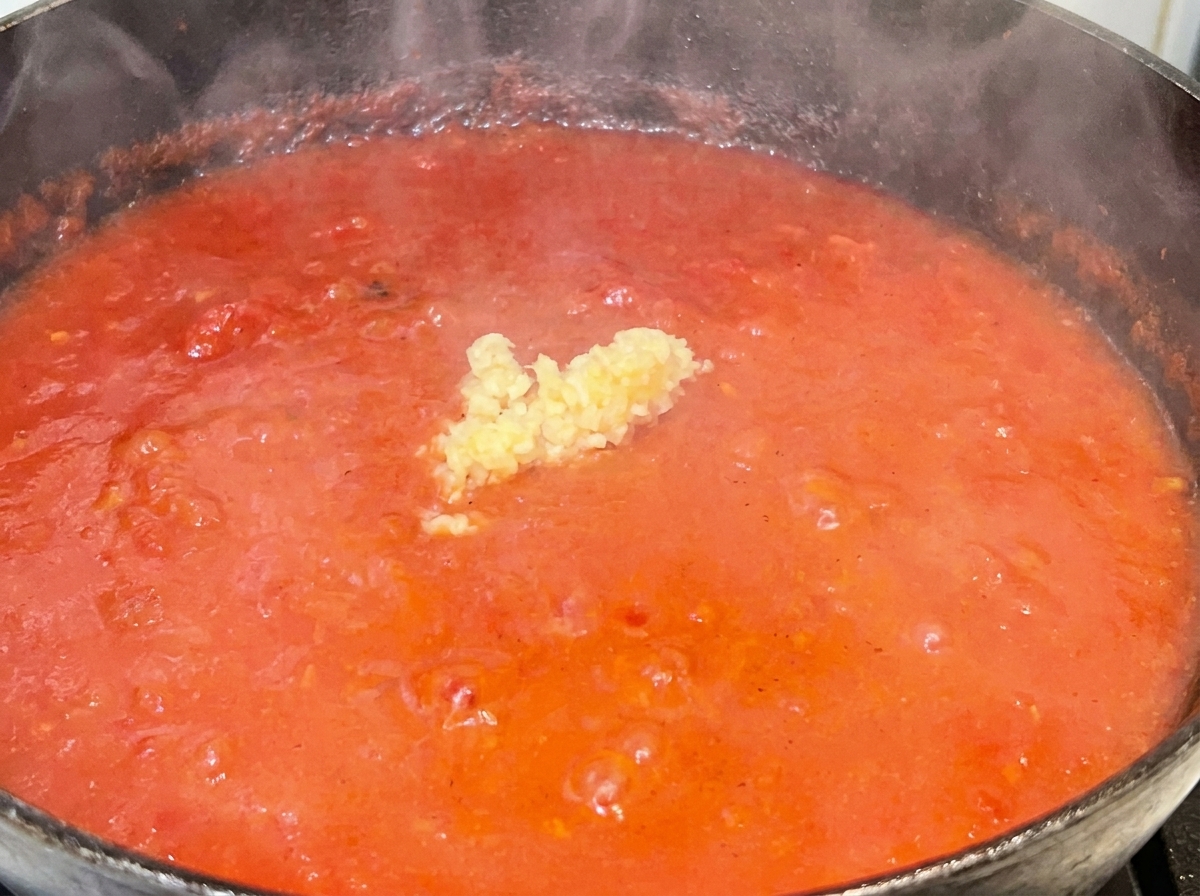Ein kleiner Haufen gehackter Knoblauch in der Mitte einer leuchtend roten, köchelnden Tomatensoße.