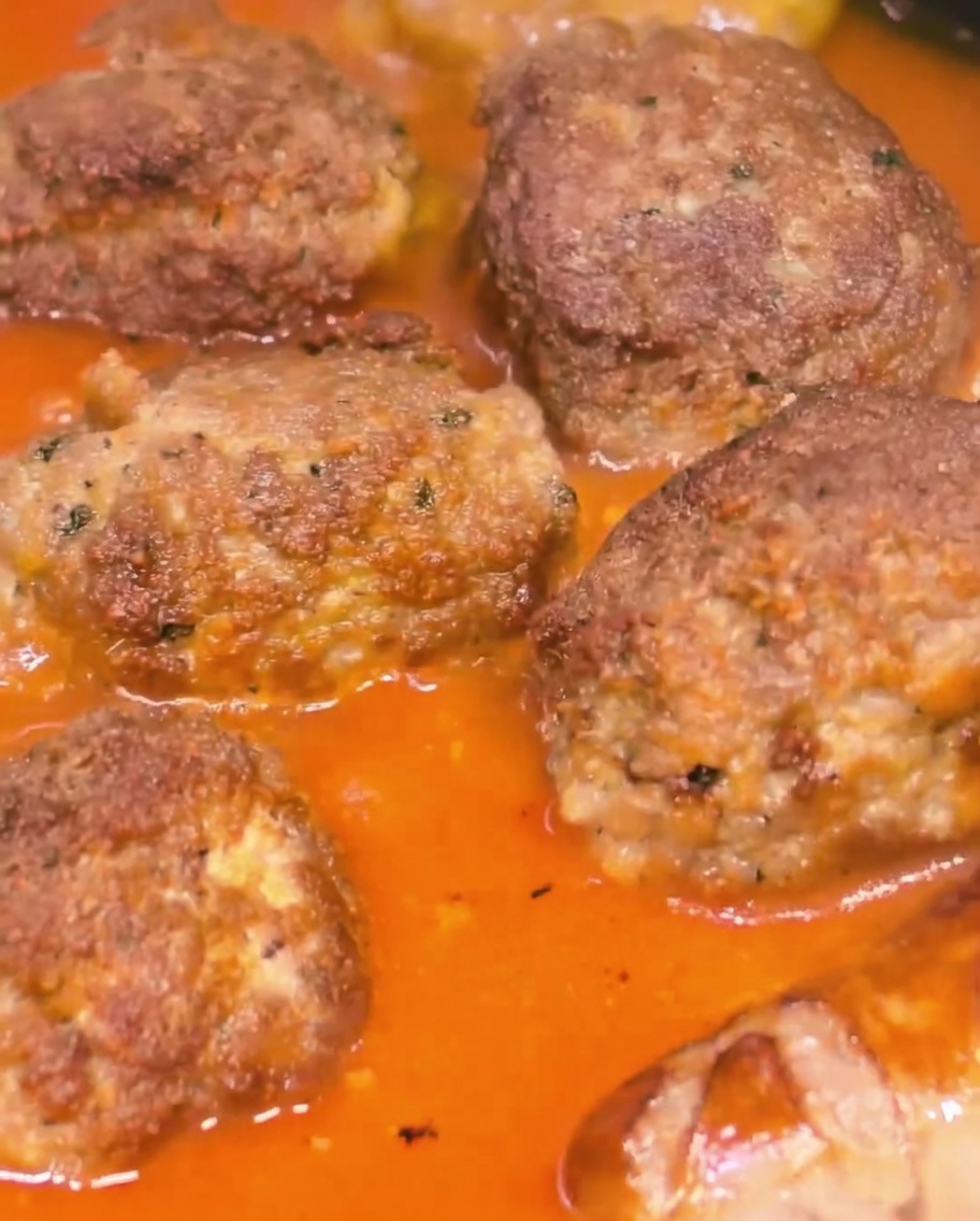 Große Hackbällchen und Würste köcheln zusammen in einer dicken Tomatensoße.