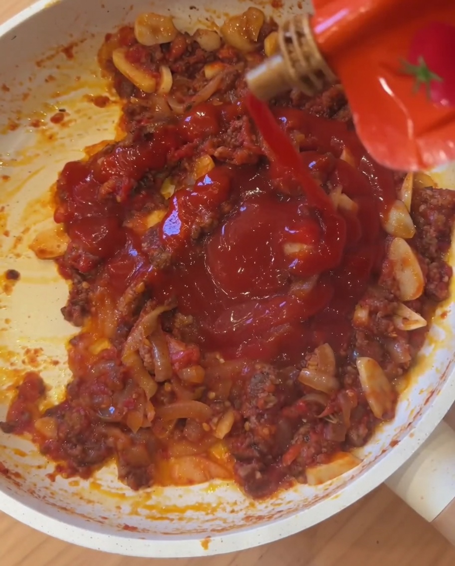 Mexikanische Scharfsauce wird in die köchelnde Tomaten-Fleisch-Mischung gegossen.