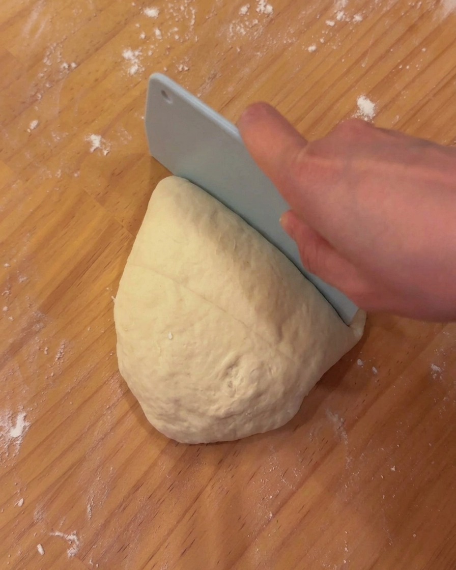 Ein portioniertes Stück Pizzateig liegt auf einem Holzbrett mit einer Teigkarte.