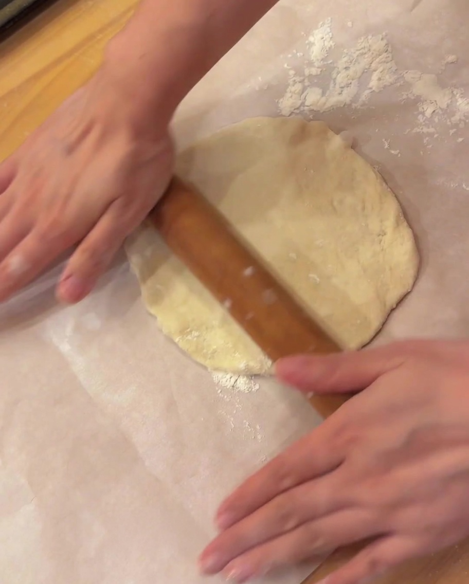 Ein Nudelholz rollt ein Stück Pizzateig auf Backpapier flach.
