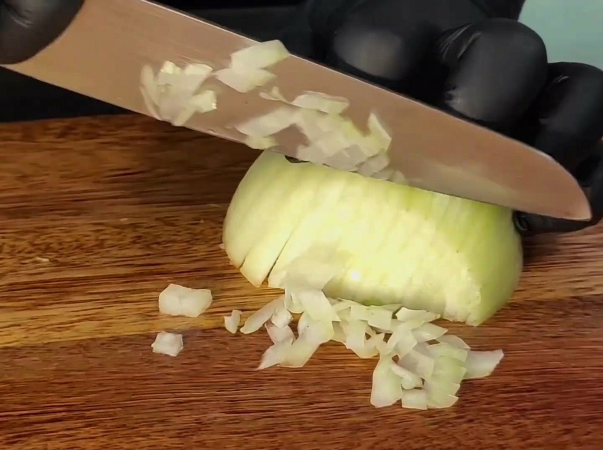 Ein Messer schneidet eine Zwiebel auf einem Holzbrett.