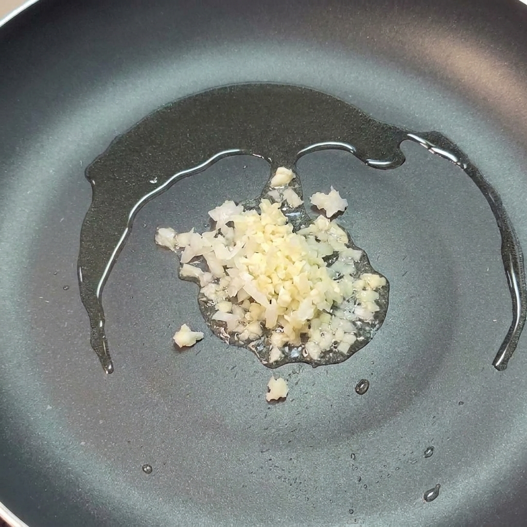 Gehackte Zwiebel und Knoblauch in einer Pfanne mit Olivenöl.