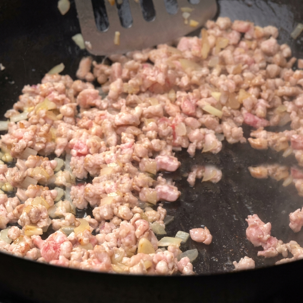 Hackfleisch bräunt in einer Pfanne zusammen mit gewürfelten Zwiebeln und wird umgerührt.