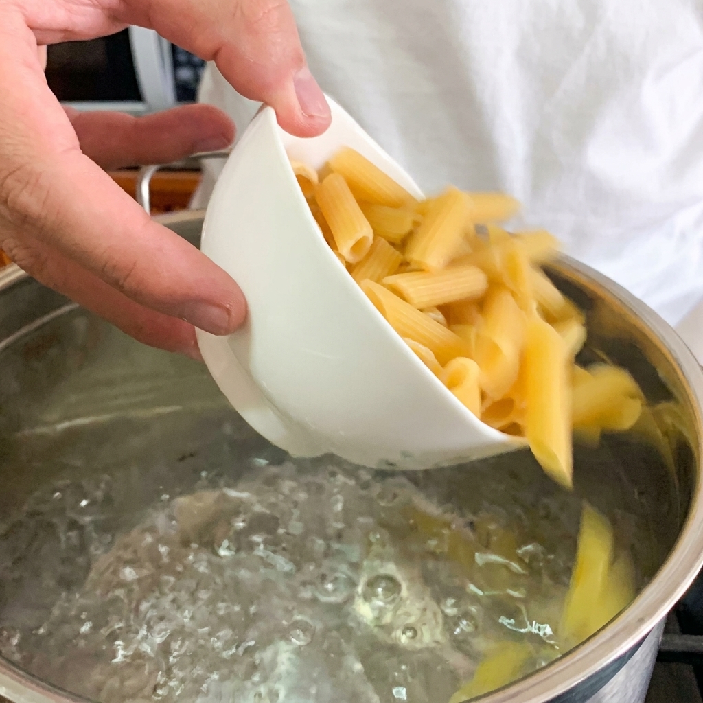 Eine Nahaufnahme eines pochierten Eies, das vorsichtig auf eine Portion cremige Penne gelegt wird.