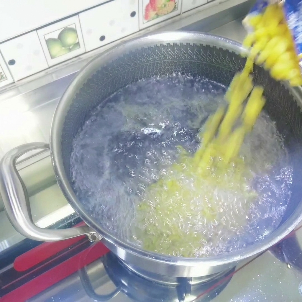 Trockene gelbe Makkaroni werden aus einer Packung in einen Edelstahltopf mit sprudelnd kochendem Wasser geschüttet.