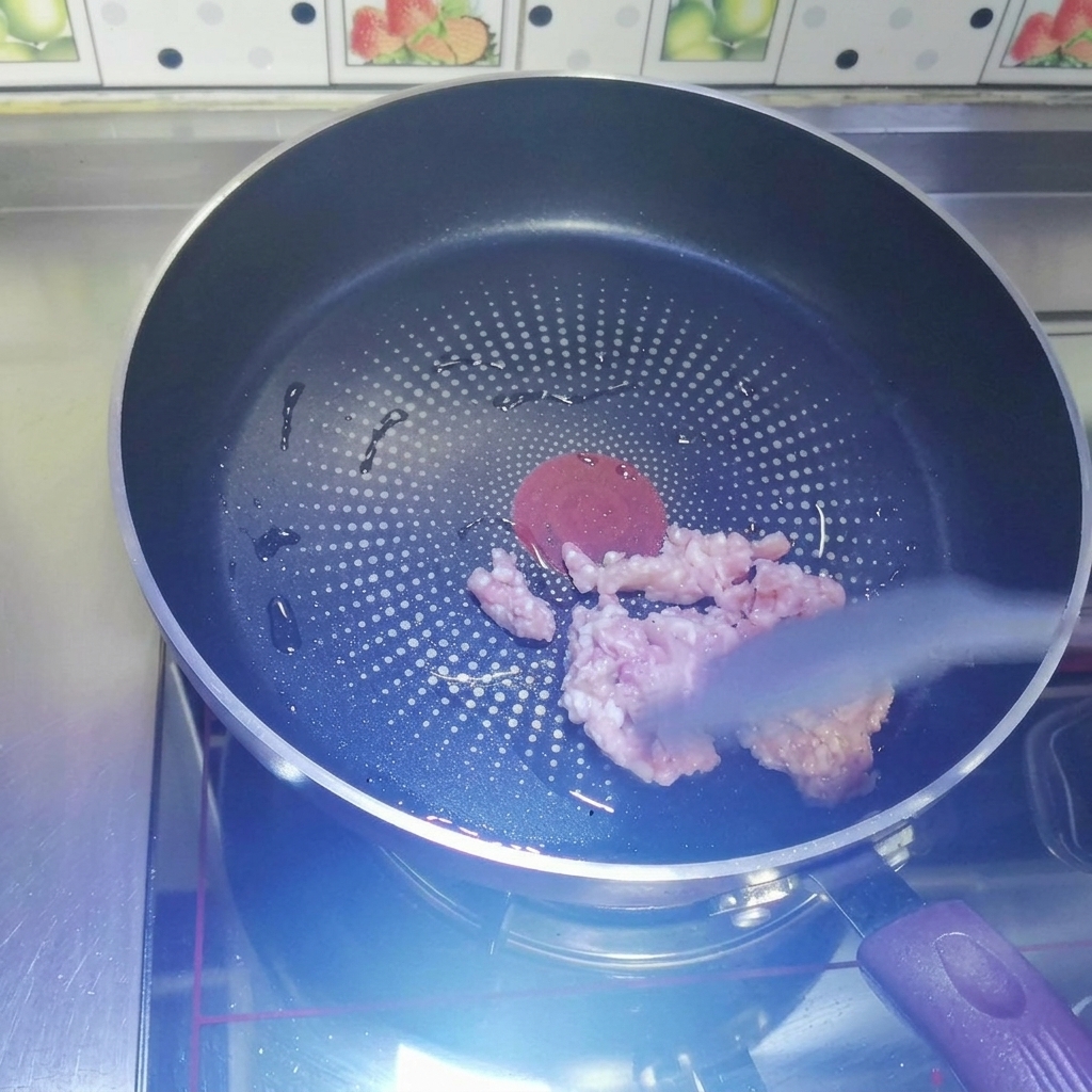 Rohes Hackfleisch wird in einer erhitzten, dunklen, beschichteten Pfanne mit einem grauen Silikonspatel angebraten.