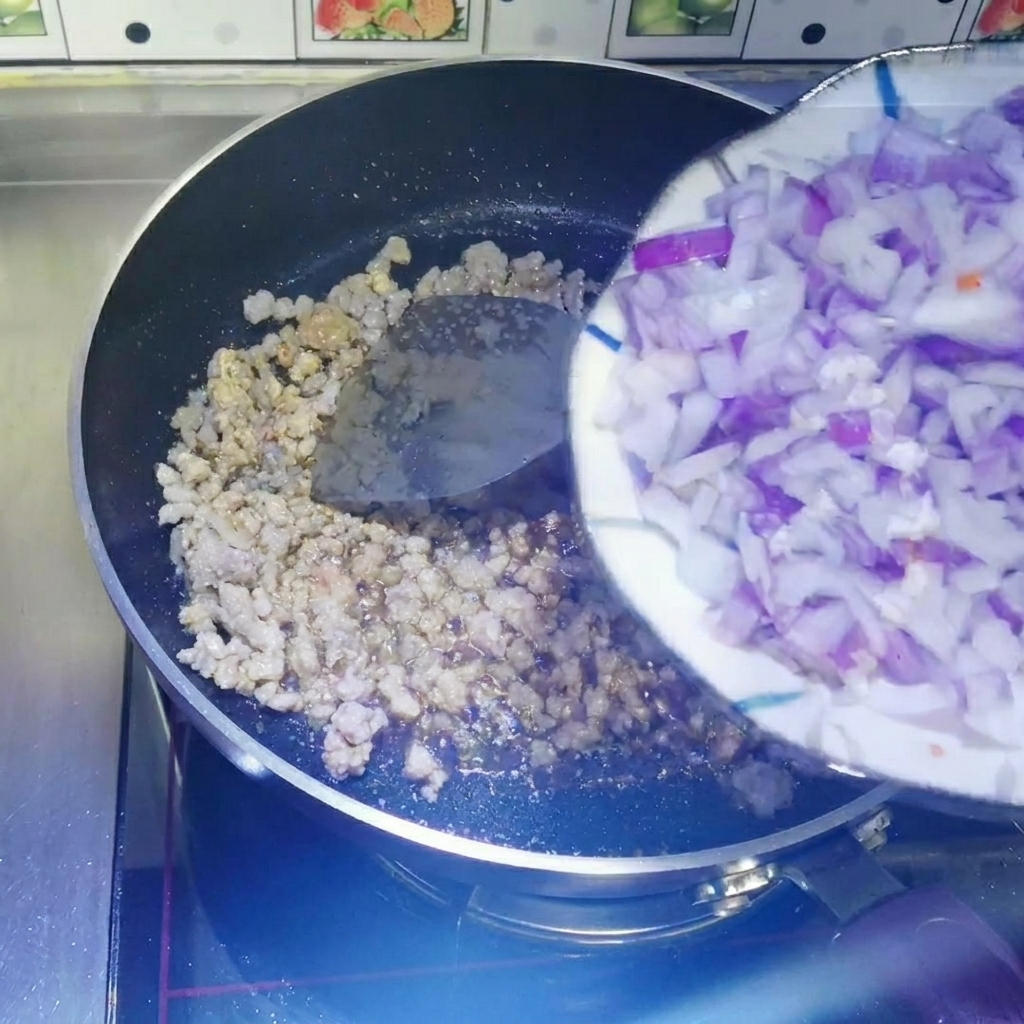 Gewürfelte rote Zwiebeln werden von einem weißen teller direkt in eine beschichtete Pfanne mit gebratenem Hackfleisch geschabt.