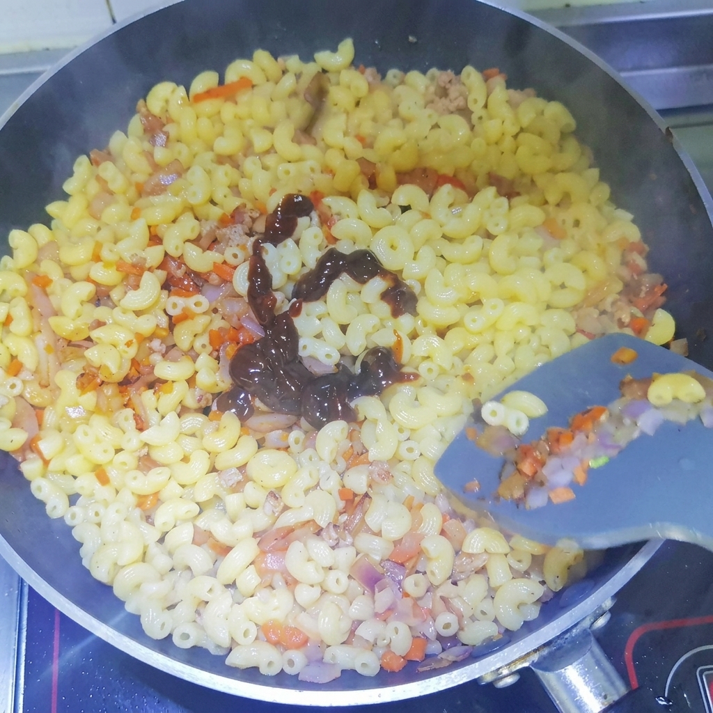 Dunkle Schwarze-Pfeffer-Sauce wird in einer Spirale über die gekochten Makkaroni in der Pfanne gegeben.