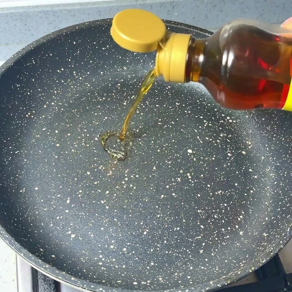 Klares Sesamöl wird aus einer Flasche in eine dunkle, gesprenkelte Pfanne gegossen.