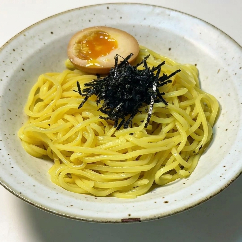 Angerichtete Ramen-Nudeln, belegt mit einer Handvoll schwarzem Nori-Seetang und einem halbierten Ei mit flüssigem Eigelb.