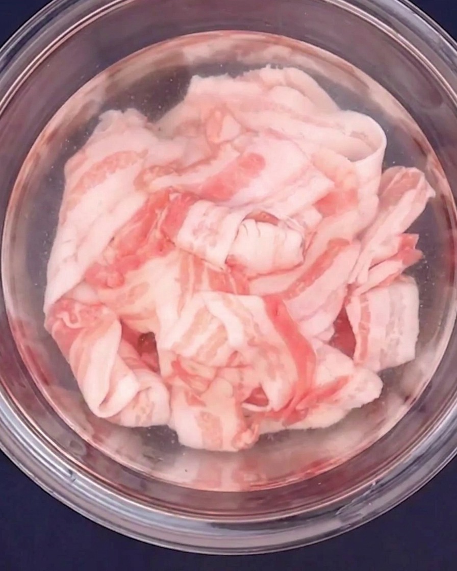 Dünn geschnittener Schweinebauch wird in einer Glasschüssel mit heißem Wasser blanchiert.