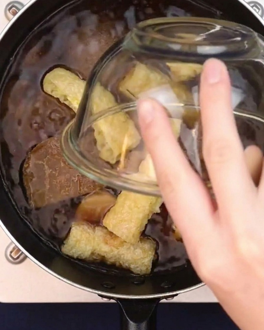 Frittierte Tofutaschen werden in einen Topf mit köchelnder japanischer Currybrühe gegeben.