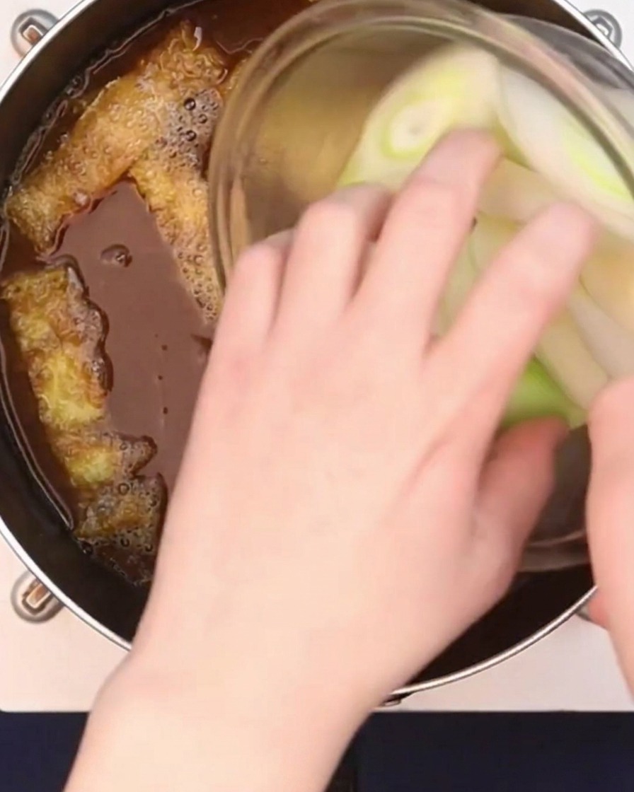 Diagonal geschnittene, große Frühlingszwiebeln werden zu einer köchelnden Currybrühe hinzugefügt.