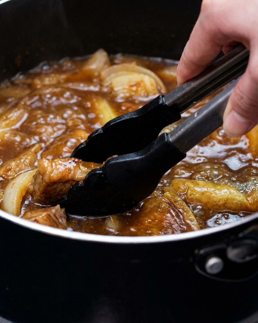 Ein Topf mit Currybrühe, Tofu und Frühlingszwiebeln wird mit einer Zange umgerührt.