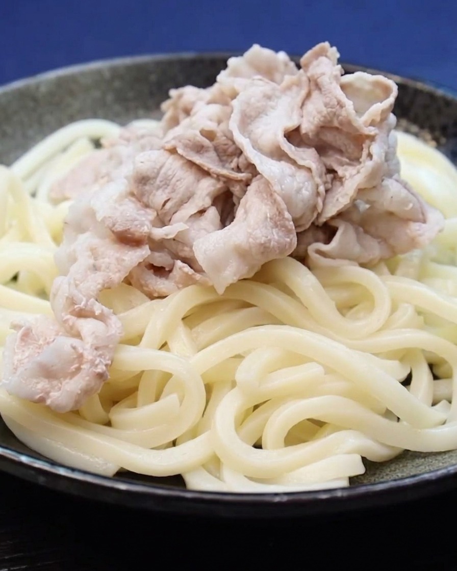Gekochte Schweinebauchscheiben werden auf ein Bett aus Udon-Nudeln gelegt.