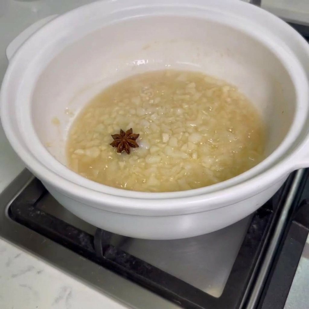 Sternanis und rohe Hähnchenflügel werden in einen Topf mit angebratenen Zwiebeln und Knoblauch gegeben.