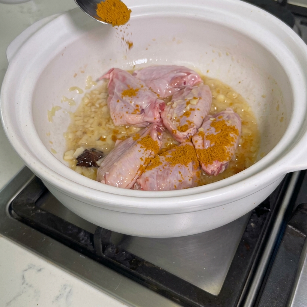 Currypulver wird über Hähnchenflügel in einem Topf gestreut.