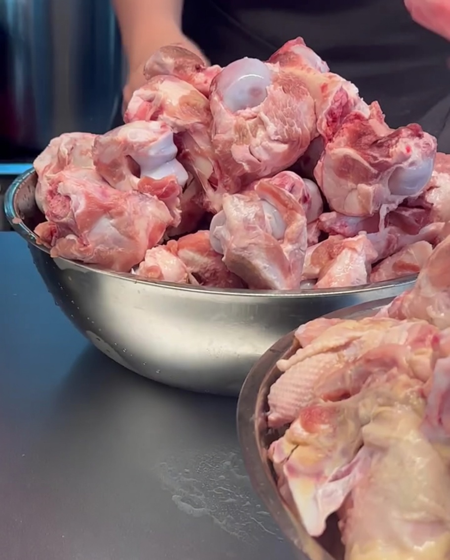 Rohe Schweineknochen und Hühnerkarkassen in einem großen Metalltopf.