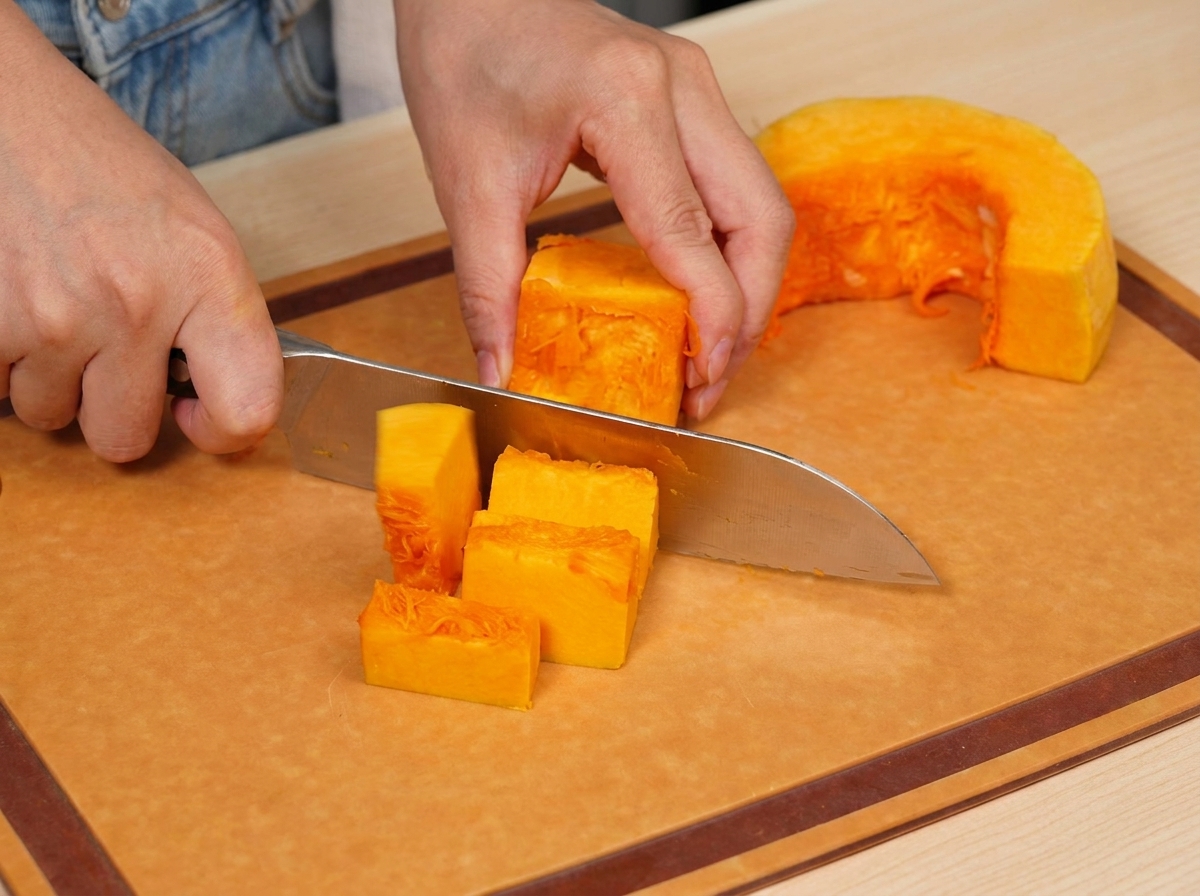 Frischer, orangefarbener Kürbis wird vorsichtig in kleinere, gleichmäßige Würfel auf einem Holzschneidebrett geschnitten.