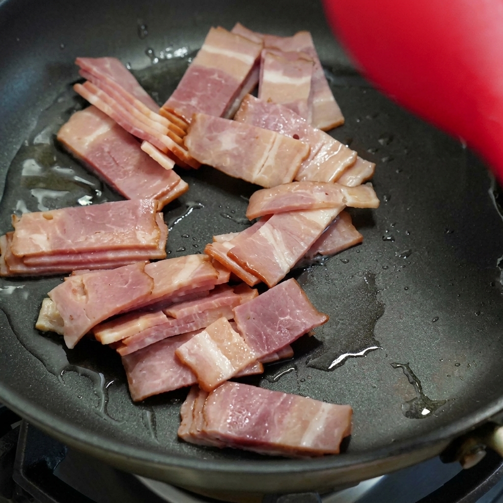 Speckstreifen braten und werden braun in einer schwarzen Pfanne, während sie mit einem roten Pfannenwender gerührt werden.