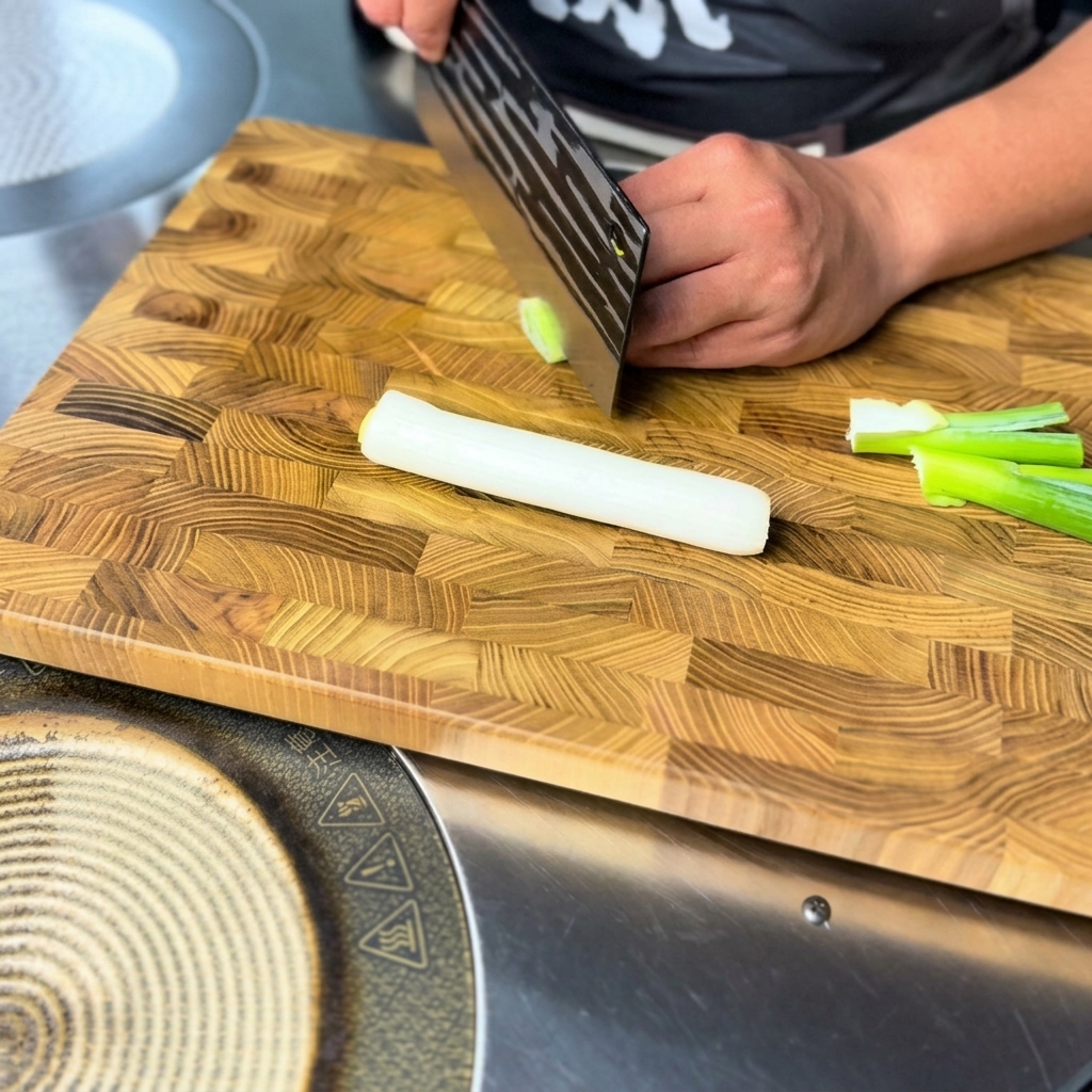 Fein gehackte Frühlingszwiebeln liegen bereit auf einem Holzschneidebrett.