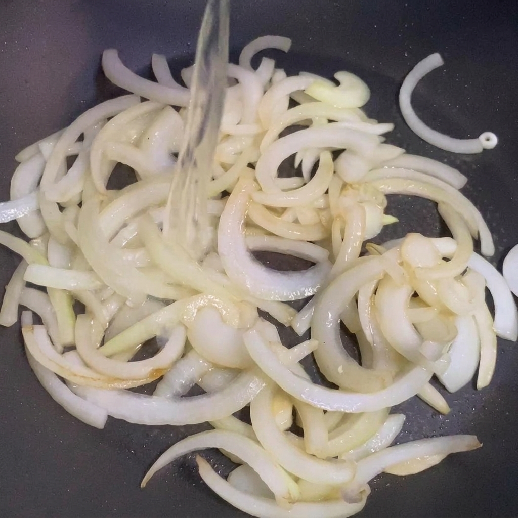 Sake wird in eine Pfanne mit angebratenen Zwiebeln gegossen.