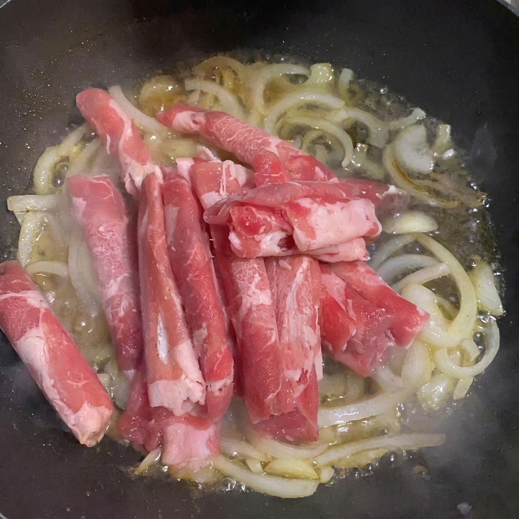 Dünne Rindfleischscheiben in der Pfanne mit Zwiebeln und Wasser.