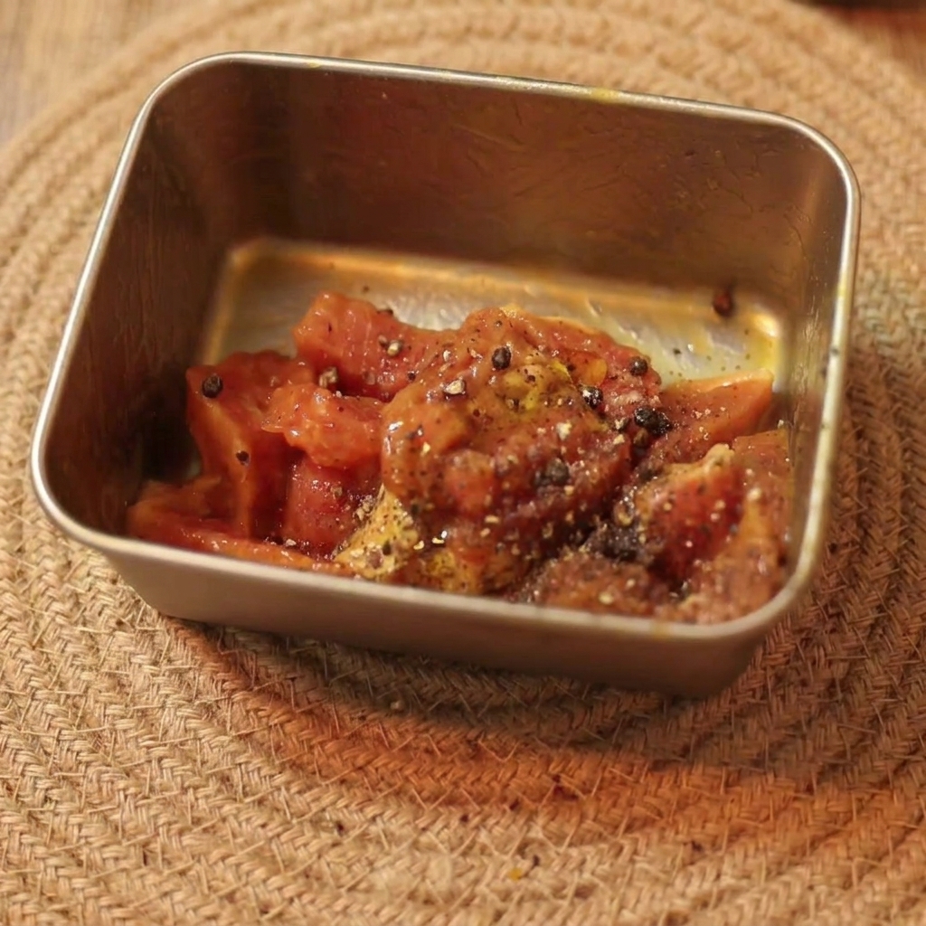Mariniertes, rohes, geschnittenes Rindfleisch, gewürzt mit schwarzem Pfeffer und Öl, in einem kleinen rechteckigen Behälter.