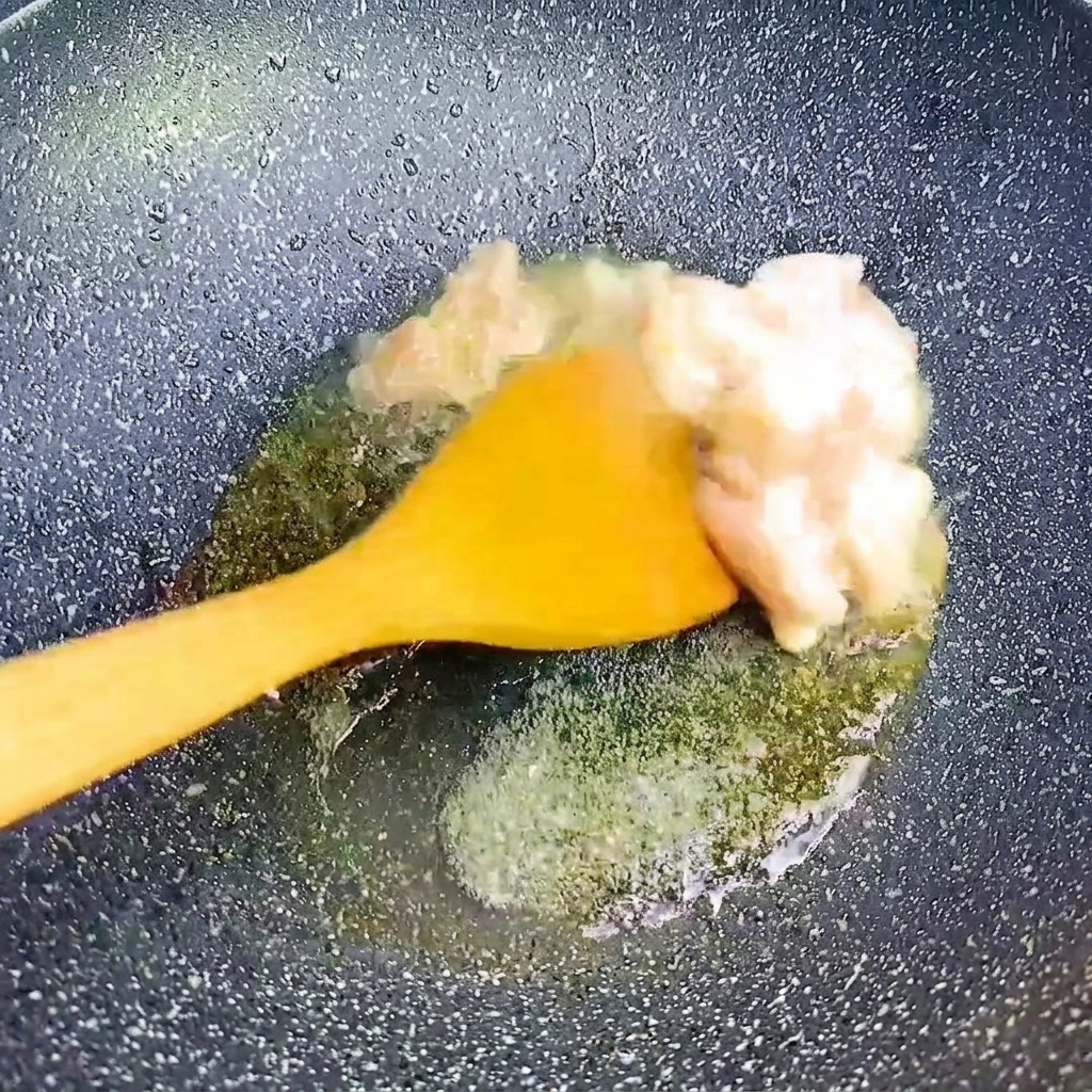 Kleine Stücke Schweinebauch werden mit einem gelben Pfannenwender in einer heißen, dunklen Pfanne angebraten.